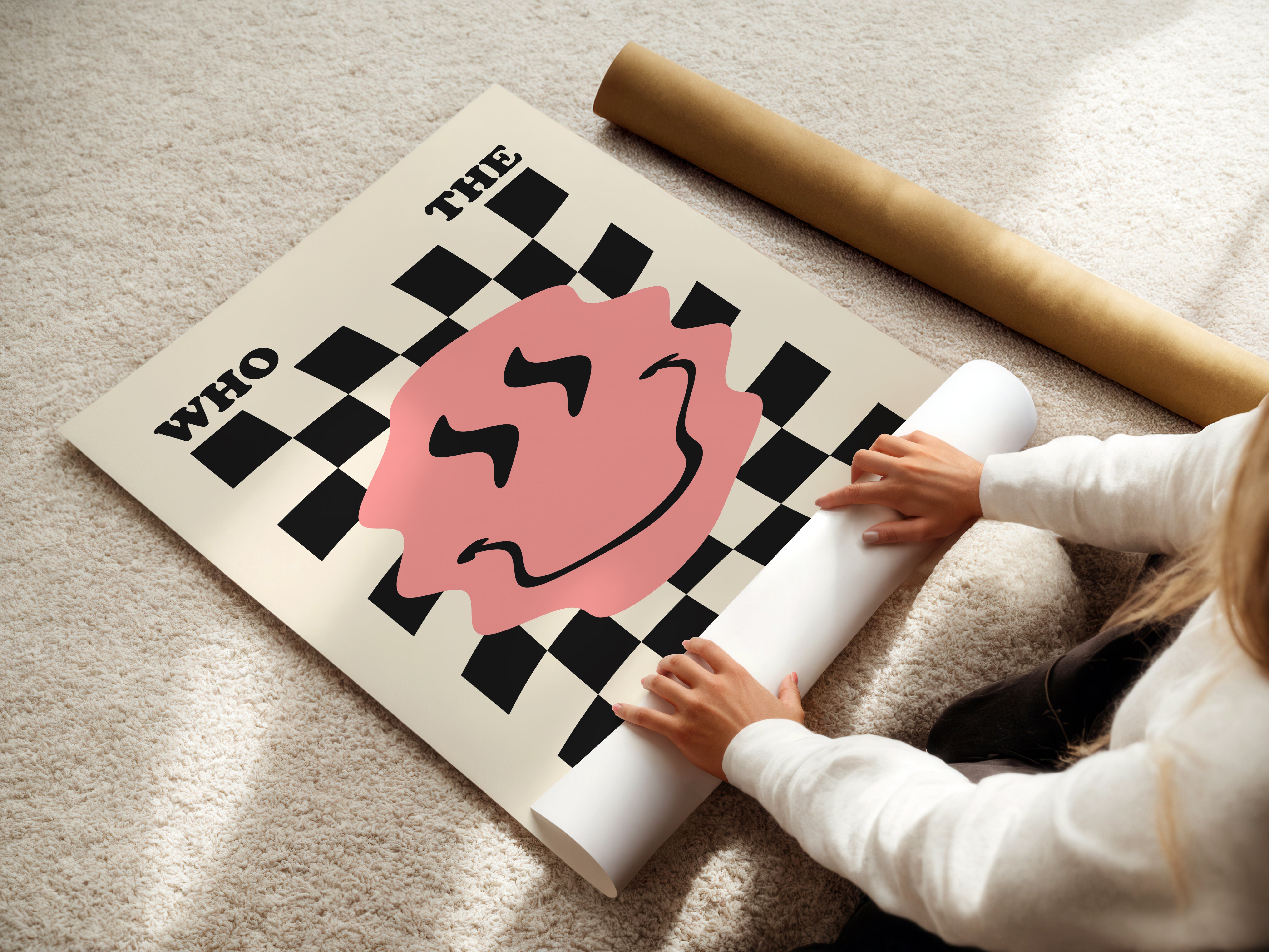 Person unrolling a large poster with a checkered design and pink circle on a light-colored floor.