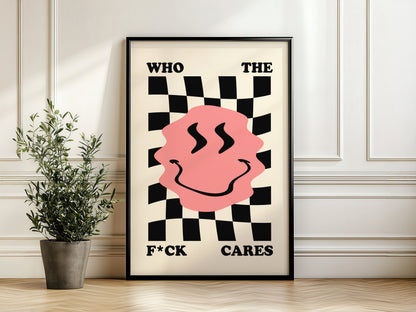 Framed poster with a pink face and text on a checkered background, placed on a wooden floor with a plant.